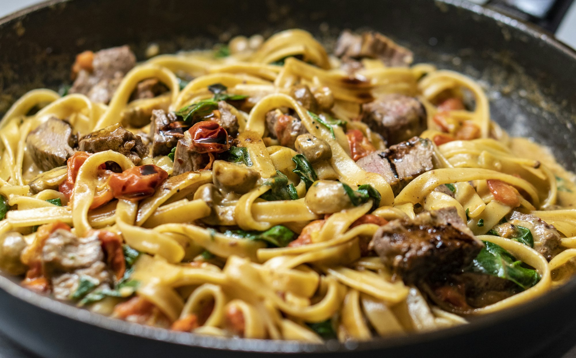Fresh tagliatelle with braised beef in a dark iron pan