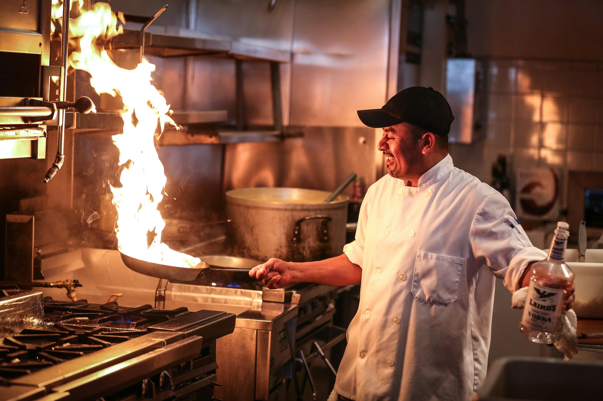 A chef working a flaming pan in a dark professional kitchen